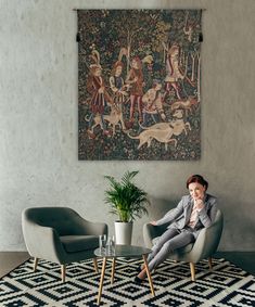 a woman sitting on a chair in front of a painting and potted plant next to a glass table