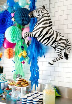 a party with zebras and balloons hanging from the ceiling, plates on the table