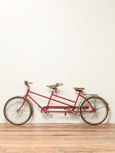 a red bike parked against a white wall in front of a wood floor and wooden floors