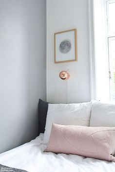 a bed with white sheets and pink pillows in a small room next to a window