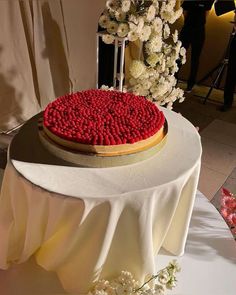 a cake with red frosting is on a white tablecloth and has flowers in the background