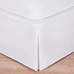 a white bed skirt on top of a wooden floor