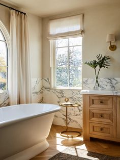 a white bath tub sitting under a window next to a wooden cabinet and counter top