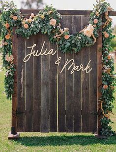 a wooden sign with flowers and greenery on it that says julia & mark in gold lettering