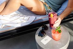 a woman is laying on the beach with a drink in her hand and strawberries