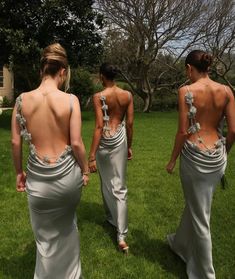 three women in long dresses are walking through the grass with their back to the camera