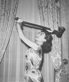 an old photo of a woman holding a bat over her head while standing in front of curtains