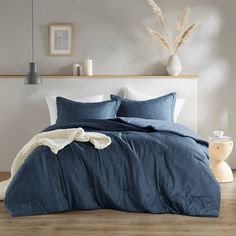 a bed with blue linens and pillows in a white room next to a plant