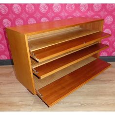 a wooden shelf with three drawers on top of it in front of a pink wall