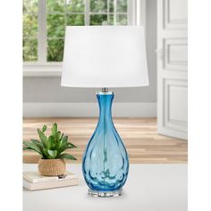 a blue glass table lamp sitting on top of a white table next to a potted plant