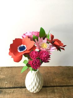 a white vase filled with flowers on top of a wooden table