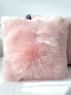 a pink fluffy pillow sitting on top of a white couch next to a black cat