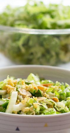 a white bowl filled with broccoli salad next to another bowl full of lettuce