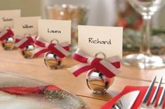 place card holders with red ribbon and bells on them sitting on a table next to silverware