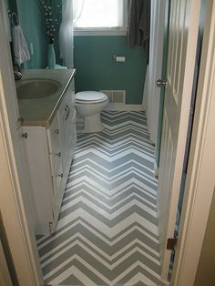 a bathroom with blue walls, white cabinets and gray chevron rugs on the floor