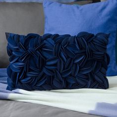 two blue pillows sitting on top of a bed next to a blanket and pillow case