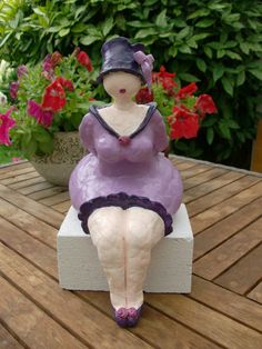 a figurine sitting on top of a wooden table next to potted flowers