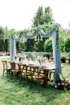 an outdoor dining table set up with blue drapes and greenery