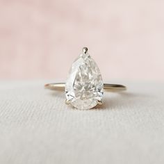 a pear shaped diamond ring sitting on top of a white cloth covered surface with a pink background