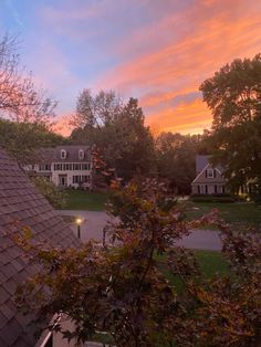 the sun is setting over a house and trees in front of it, as seen from an upstairs window