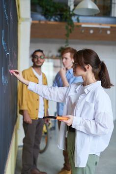 a woman writing on a blackboard while two other people watch