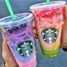 two starbucks drinks with strawberries and blueberries in them are being held by someone's hands