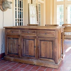 a large wooden cabinet sitting on top of a red tile floor next to a mirror