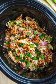 a slow cooker filled with shredded meat and green onions on a cutting board next to celery