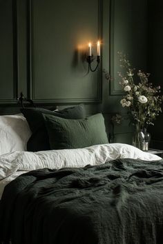 a bedroom with green walls and white linens on the bed is lit by two wall sconces