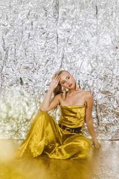 a woman in a gold dress sitting on the floor with her hand to her face