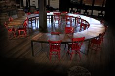 a large circular table with red chairs around it in the middle of a dark room