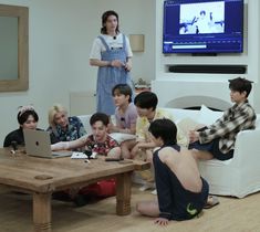 a group of young people sitting around a wooden table in front of a laptop computer