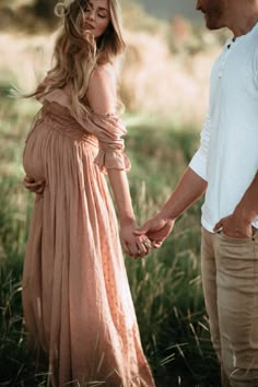 a pregnant woman in a long dress holding hands with a man standing next to her