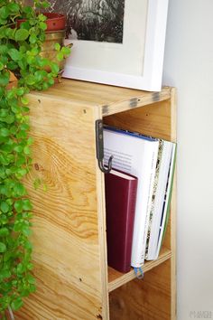 a wooden shelf with books and plants on it next to a white framed photo in the corner