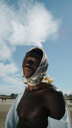 a man wearing a headscarf standing on the beach under a blue cloudy sky