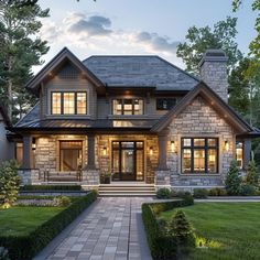 a large house with lots of windows and lights on it's front porch, surrounded by greenery