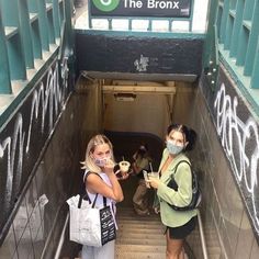 two women wearing face masks standing at the bottom of an escalator with graffiti on it