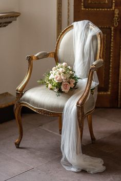 a bouquet of flowers is sitting on an old chair with a white veil draped over it