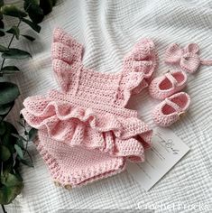 a pink crocheted outfit and booties on a white blanket