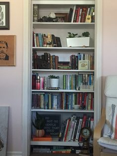 a bookshelf filled with lots of books next to a chair and pictures on the wall