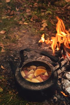 a pot sitting on top of a fire next to a campfire filled with food