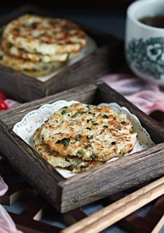 some food is sitting in small wooden trays next to chopsticks and a cup