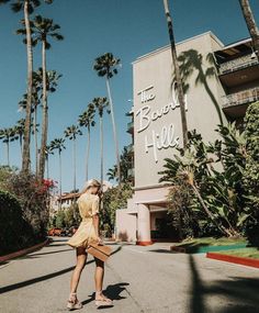 a woman walking down the street in front of a hotel with palm trees on both sides