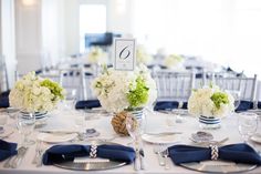 the table is set with silverware and blue napkins, white flowers and greenery