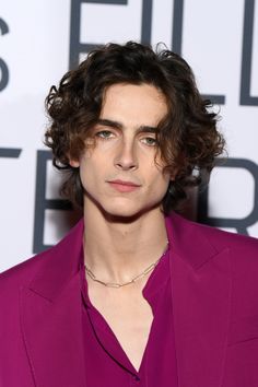 a young man with curly hair wearing a purple suit and diamond necklace at an event