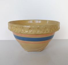 a yellow and blue striped bowl sitting on top of a table next to a white wall