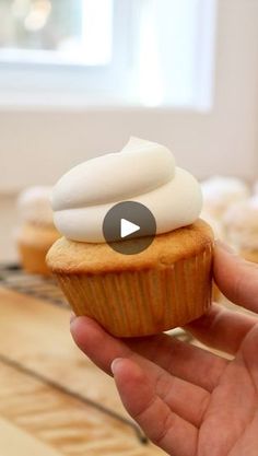 a hand holding a cupcake with white frosting