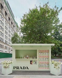 a small display case on the sidewalk in front of a tall building with trees and flowers