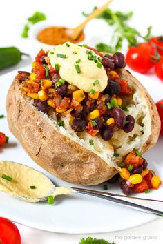 a baked potato filled with black beans, corn and cheese on a white plate next to chips