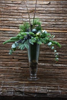 a vase filled with flowers and greenery on top of a wooden table next to a bamboo wall